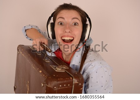 joyful woman in headphones with a suitcase on a light background portrait