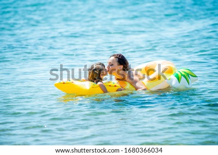 Mom and little 3 year old daughter swim together on the sea in yellow inflatable circles and kiss