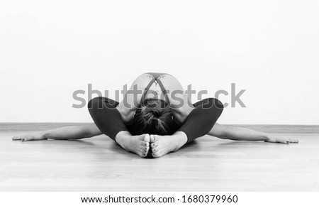 Black and white photography of a blonde woman on the floor doing the Supta Kurmasana yoga position indoors