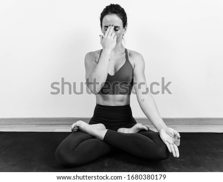 Unsaturated photography of a woman meditating and doing the Pranayama anuloma viloma yoga position on the floor of a room