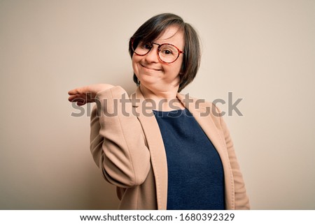 Young down syndrome business woman wearing glasses standing over isolated background smiling cheerful presenting and pointing with palm of hand looking at the camera.