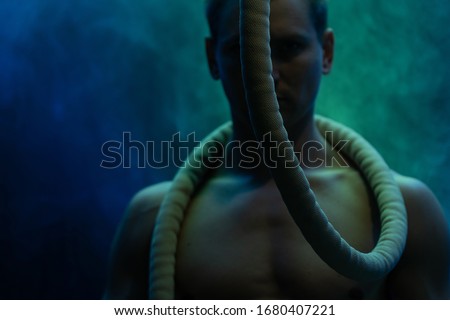 Muscular male circus artist with Cord Lisse on black an smoked background