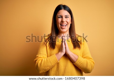 Young beautiful woman wearing casual sweater over yellow isolated background praying with hands together asking for forgiveness smiling confident.