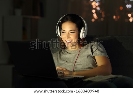 Happy woman in the night watching media on laptop sitting on a sofa in the living room at home Royalty-Free Stock Photo #1680409948