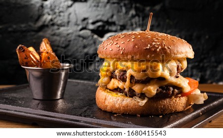 Big cheeseburger with lots of cheese. Stock photo side view of a cheeseburger on a black brick wall background.