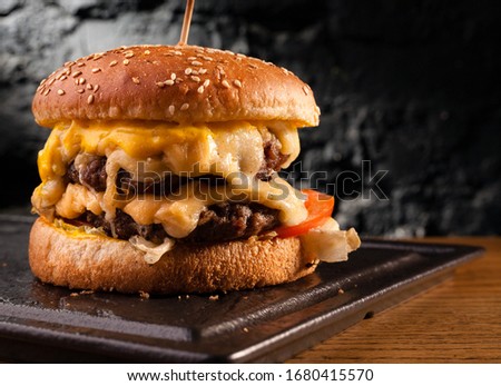 Big cheeseburger with lots of cheese. Stock photo side view of a cheeseburger on a black brick wall background. Royalty-Free Stock Photo #1680415570