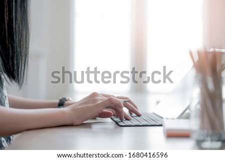 Cropped shot of woman hand holding pen and typing on tablet keyboard while sitting and working at home office.