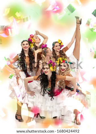 Surprised. Beautiful young women in carnival, stylish masquerade costume with feathers on white background in neon light, flying confetti. Holidays celebration, dancing, fashion. Festive time, party.