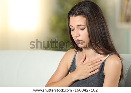 Girl having respiration problems touching chest sitting on a couch in the living room at home Royalty-Free Stock Photo #1680427102