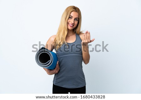 Young sport woman going to yoga classes while holding a mat over isolated white background inviting to come with hand. Happy that you came