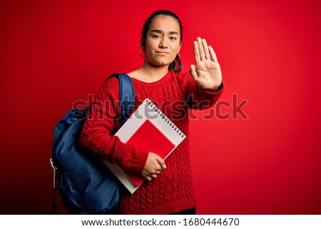 Young beautiful asian student woman wearing backpack standing over isolated red background with open hand doing stop sign with serious and confident expression, defense gesture