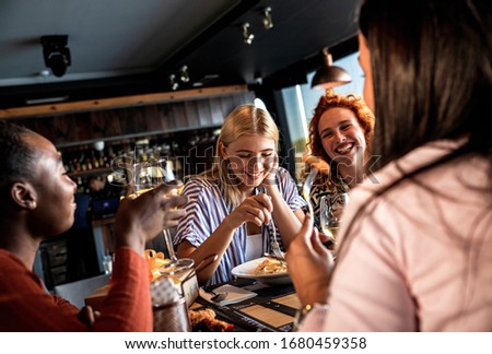 Group of young female friends having fun in restaurant, talking and laughing while dining at table.	
