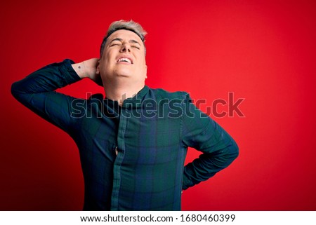 Young handsome modern man wearing elegant green shirt over red isolated background Suffering of neck ache injury, touching neck with hand, muscular pain