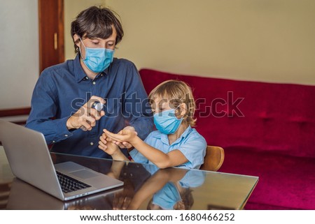 Boy studying online at home using laptop. Father helps him learn. Father and son in medical masks and sanitizer to protect against coronovirus. Studying during quarantine. Global pandemic covid19