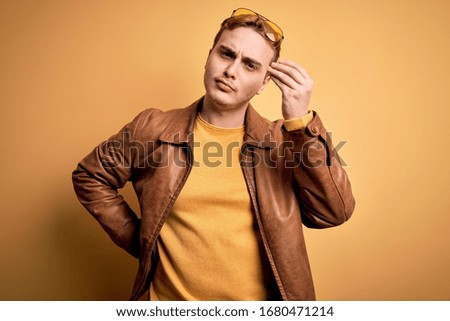 Young handsome redhead man wearing casual leather jacket over isolated yellow background Doing Italian gesture with hand and fingers confident expression