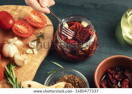 Female hand puts the forked tomatoes into a glass jar with a fork. Cooking canned jerky tomatoes with spices
