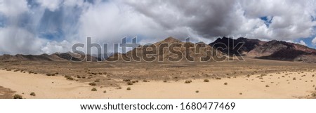 Panorama of bare mountains in the valley of the river Murghab with dark rain clouds near the village of Murghab, Tajikistan at the Pamir Highway.