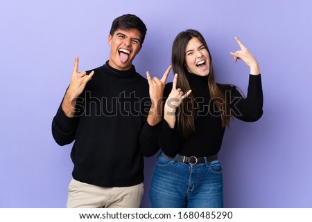 Young couple over isolated purple background making rock gesture