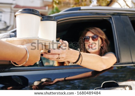 Waiter giving disposable tray with two cups of take out coffee to pretty smiling female driver Royalty-Free Stock Photo #1680489484