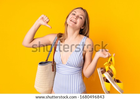 Teenager Ukrainian girl holding summer sandals isolated on yellow background proud and self-satisfied