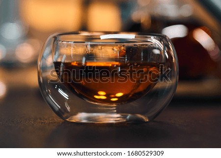 Transparent bowl with black tea on a wooden table. Blurred background of bright lights. Horizontal picture.