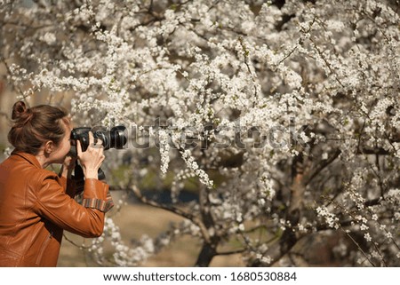 A girl photographer photographs the lush flowering of a tree in spring. The concept of a hobby, hobby as a business, freelance.