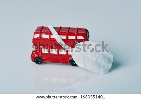 a miniature of a red double-decker bus, an icon of the United Kingdom, and a face mask on an off-white background