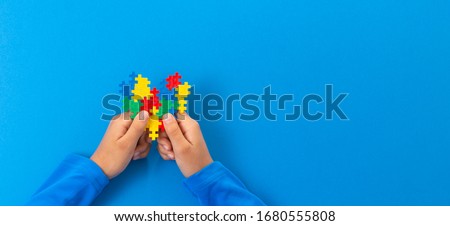 World autism awareness day concept. Child hands holding colorful puzzle heart on blue background