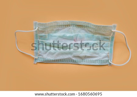 Used green surgical face mask with cosmetic stains, lipstick marks isolated on color background, cause of the spread of germs, virus or bacteria. problem of unhygienic disposal of infectious waste. Royalty-Free Stock Photo #1680560695
