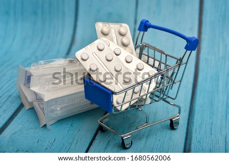 Cart with medicines, pills, antibiotics, vitamins, antiviral agents in a consumer basket on a background of syringes.