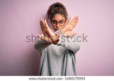 Young beautiful african american girl wearing sweater and glasses over pink background Rejection expression crossing arms doing negative sign, angry face