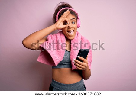 Young african american sportswoman playing tennis using racket over isolated pink background with happy face smiling doing ok sign with hand on eye looking through fingers