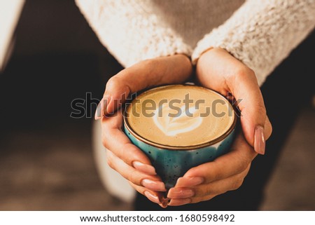 Beautiful female hands holding a blue cup with cappuccino.