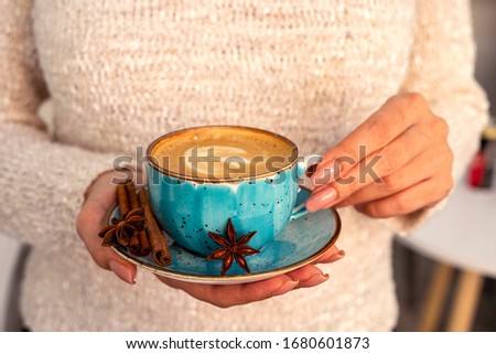 Beautiful female hands holding a blue cup with cappuccino.