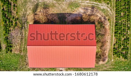Vertical aerial view of a barn with a red roof next to a tree plantation