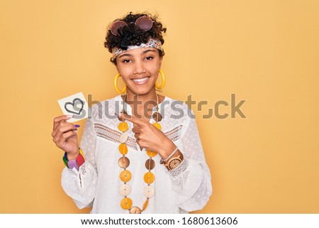 Beautiful african american afro hippie woman wearing sunglasses holding reminder with heart very happy pointing with hand and finger