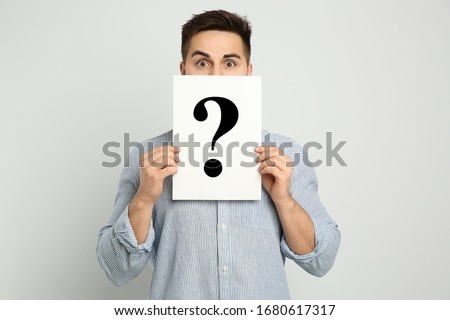 Emotional man holding question mark sign on light background Royalty-Free Stock Photo #1680617317