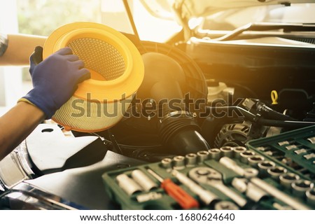 Cropped image of handsome young auto mechanic in uniform repairing car Change car air filter in auto service.selective focus. Royalty-Free Stock Photo #1680624640