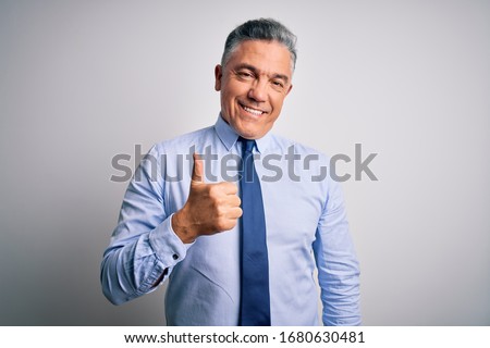 Middle age handsome grey-haired business man wearing elegant shirt and tie doing happy thumbs up gesture with hand. Approving expression looking at the camera showing success.