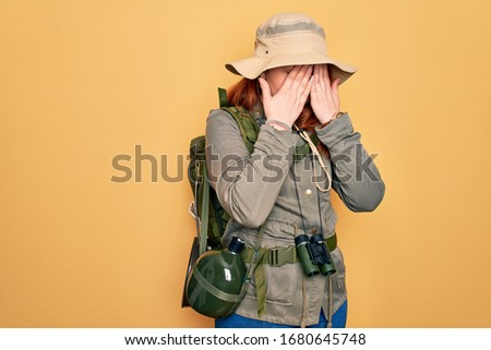 Young redhead backpacker woman hiking wearing backpack and hat over yellow background rubbing eyes for fatigue and headache, sleepy and tired expression. Vision problem