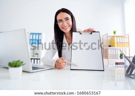 Photo of pretty professional doc lady hold clipboard with hospital contract insurance showing patient place for signature wear white lab coat sit chair office clinic indoors