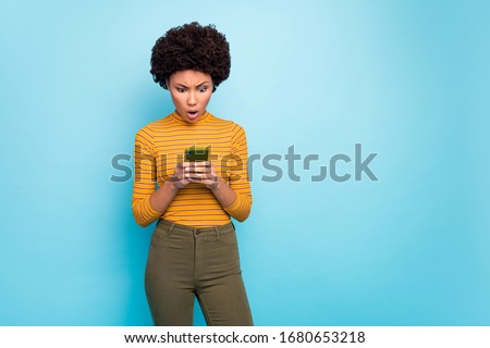 Photo of beautiful dark skin curly lady hold telephone read bad news comments open mouth epic fail wear yellow striped sweater shirt green trousers isolated blue color background