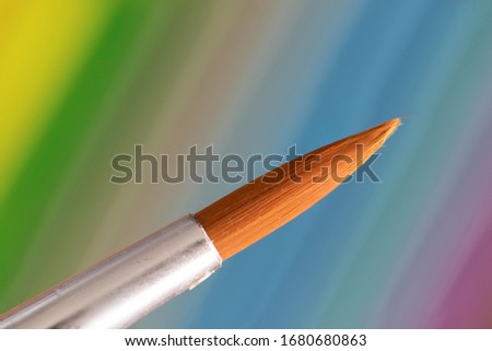 A macro portrait of a paintbrush tip in front of a colorful background. The brush hair is still together forming a nice tip.