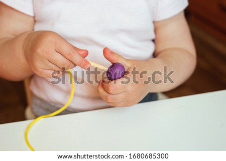 Child putting beads on a string. Bead stringing activity. Fine motor skills development. Early education, Montessori Method. Cognitive skills, children development. Close up of baby's hands. Royalty-Free Stock Photo #1680685300
