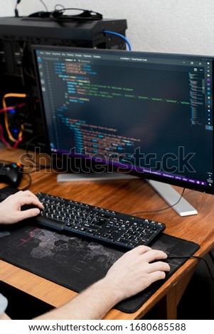 man is typing on a black keyboard. In the background there is a monitor, a mouse and a computer mat with the image of a world map
