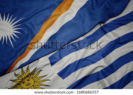 waving colorful flag of uruguay and national flag of Marshall Islands . macro