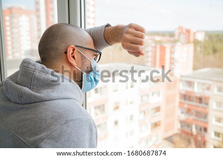 Lonely man in medical mask looking through the window. Isolation at home for self quarantine. Concept home quarantine, prevention COVID-19. Coronavirus outbreak situation Royalty-Free Stock Photo #1680687874