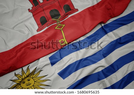 waving colorful flag of uruguay and national flag of gibraltar. macro