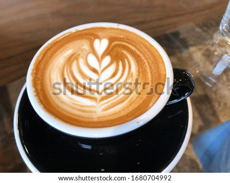 Coffee latte art in cup and heart leaf of milk froth above to drink on clear glass table background, Relaxing take a break time  for today.