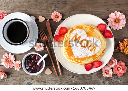 Pancakes with heart shape and MOM letters. Mothers Day breakfast concept. Overhead view table scene with a rustic wood background. Royalty-Free Stock Photo #1680705469
